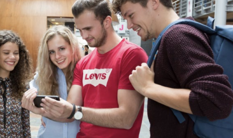 Vier studenten kijkend naar een mobiele telefoon