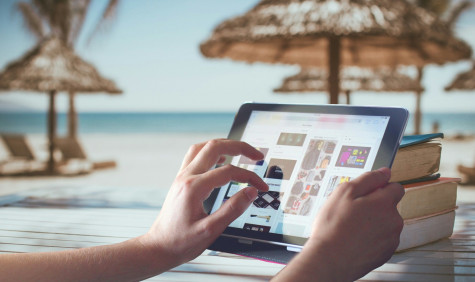 Two hands holding a tablet with beach parasols in the background