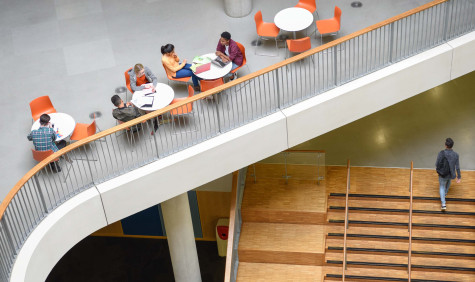 Top view of a hallway and staircase where students sit at round tables working together.