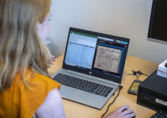 Vrouw achter laptop waarop oude tekst te zien is
