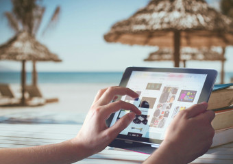 Two hands holding a tablet with beach parasols in the background