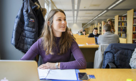 Student aan tafel met computer in bibliotheek