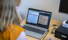 Vrouw achter laptop waarop oude tekst te zien is