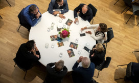 Een ronde tafel van bovenaf gefotografeerd met daaraan volwassenen die met elkaar in gesprek zijn