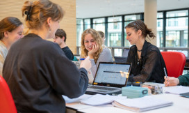 vier studentes zijn lachend aan het werk op hun laptop