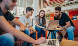 Studenten achter laptops aan lage tafels in een open ruimte in een instelling