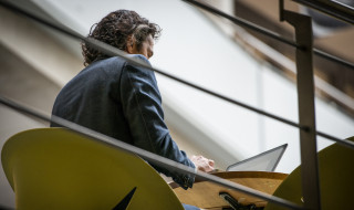 Man achter computer aan tafel op verhoging, foto van verdieping lager genomen