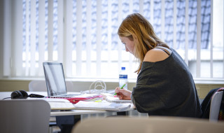 Studente aan het werk achter computer met veel documenten en aantekeningen voor zich