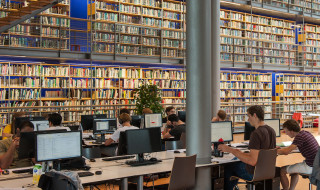 Open bibliotheek met hele hoge boekenwand en werkende studenten