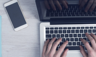 Man aan laptop met mobiel van bovenaf gefotografeerd