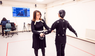Zerrin Yumak attaches sensors on a person dressed in black at the motion capture lab