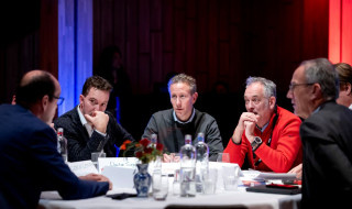 Vijf mannen aan een ronde tafel met elkaar in gesprek