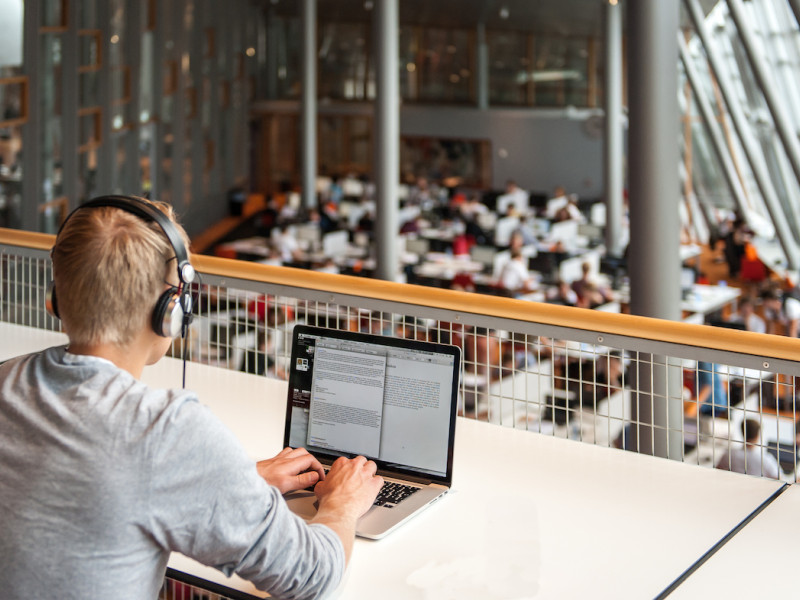 Student achter laptop in bibliotheek vanaf verhoging met koptelefoon