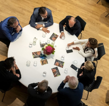 Een ronde tafel van bovenaf gefotografeerd met daaraan volwassenen die met elkaar in gesprek zijn